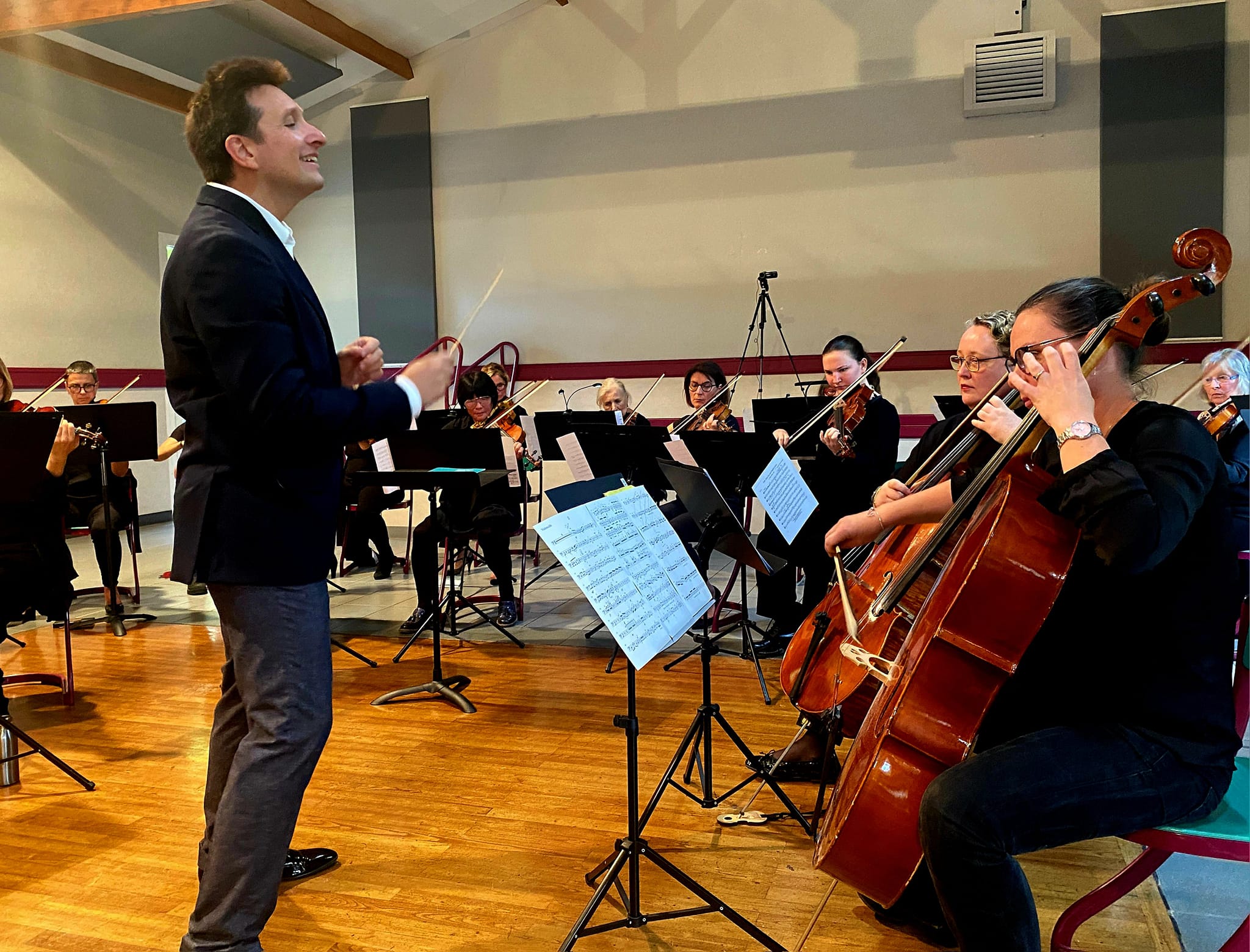 Jonathan Raspiengeas dirige un orchestre, les mains levées.